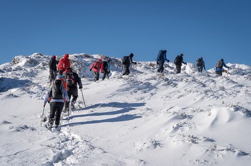 Group of hikers walking in deep snow upa hill, across a beautiful calm scenic landscape, with blue sky on a winter day